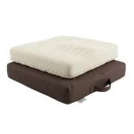 Coussin anti-escarre mousse écrue posé sur housse marron avec poignée latérale